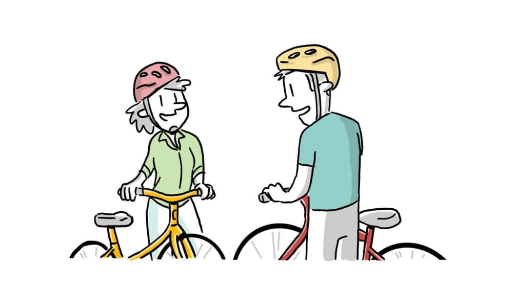 Two people stand next to their bikes, chatting with helmets on, showcasing the connection between people during a biking experience.